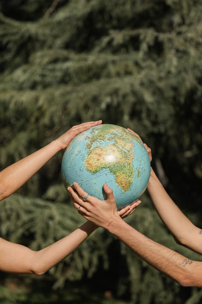 who-we-are-img Four hands holding a globe outdoors, symbolizing unity and environmental conservation.