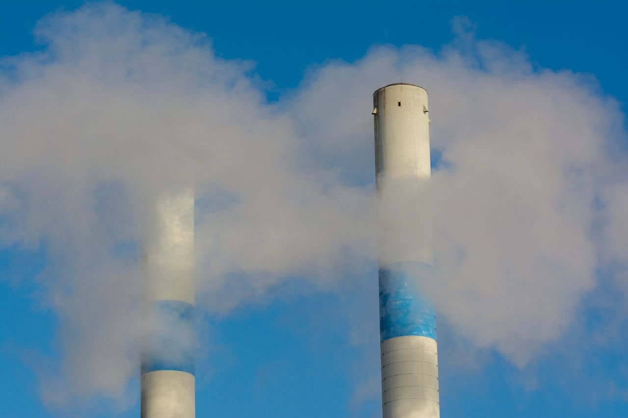 awards-img Twin industrial chimneys emitting smoke under a clear blue sky, highlighting air pollution concerns.